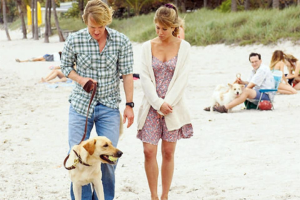 Couple walking a dog on a sandy beach in a scene from Marley & Me